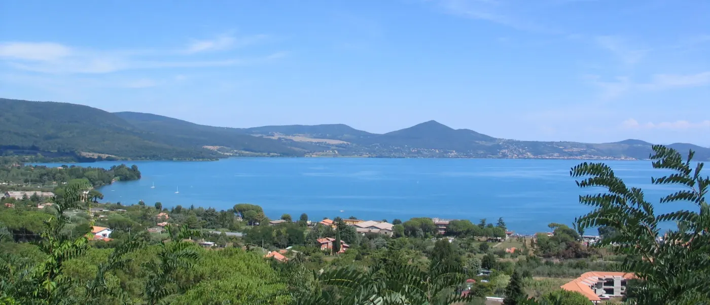 A blue volcanic lake below wooded hills, lakeside villages along the far shore
