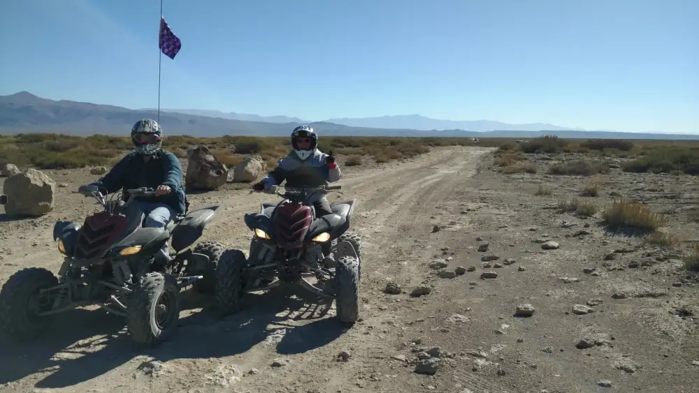 Two helmeted riders on quad bikes on a stony track