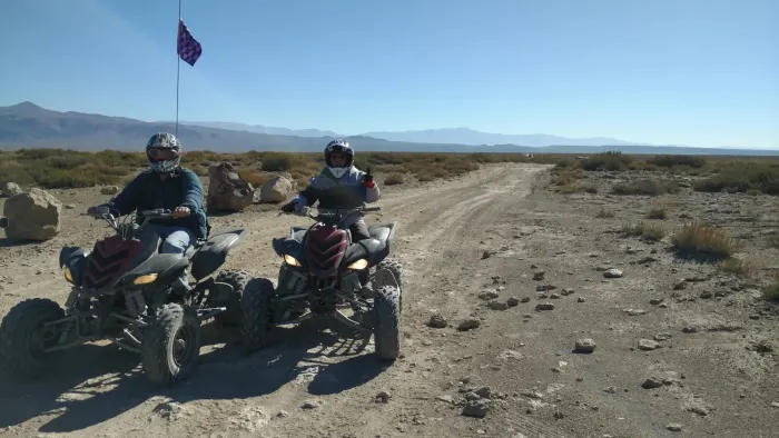 Two helmeted riders on quad bikes on a stony track