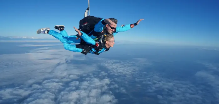 A tandem skydiving pair in freefall above the clouds