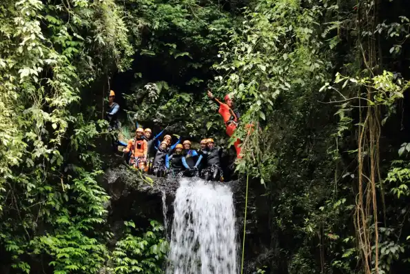 A group abseiling beside a waterfall in a canyon