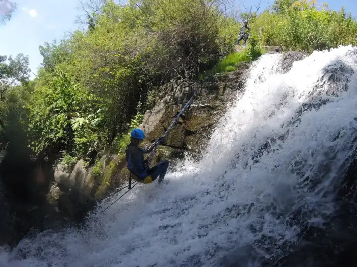 A canyoner in the water of a canyon, helmet and wetsuit on