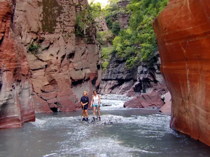 A canyoner in helmet and wetsuit descending a rope beside a waterfall
