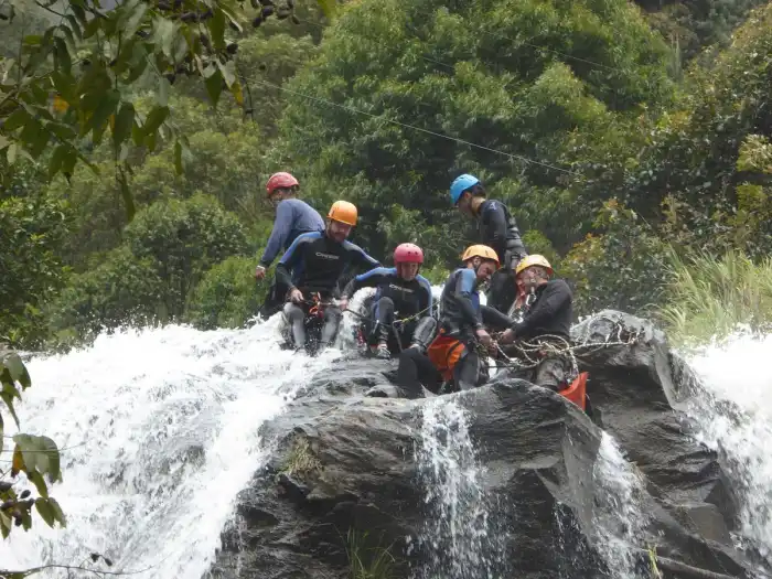 A canyoner in helmet and wetsuit descending a rope beside a waterfall