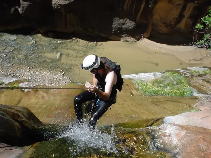 A canyoner in helmet and wetsuit descending a rope beside a waterfall