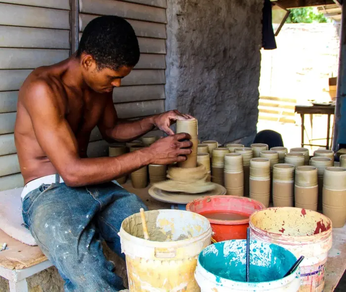 A potter shaping a pot on the wheel, finished pieces behind