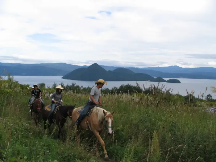 Riders on horseback on a trail above a lake