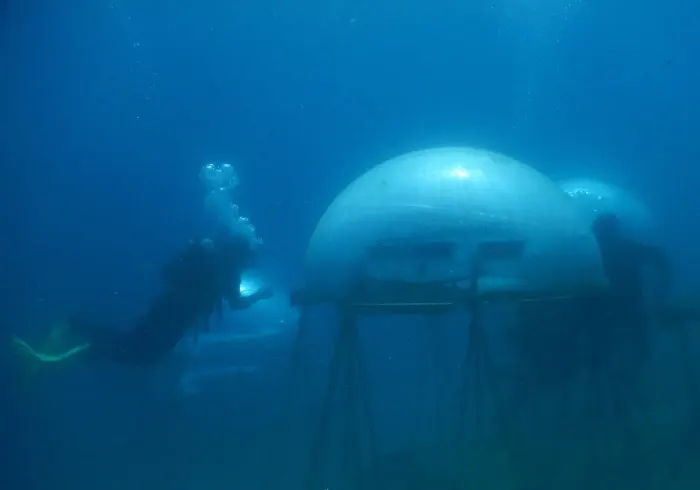 A scuba diver beside an underwater dome in blue water