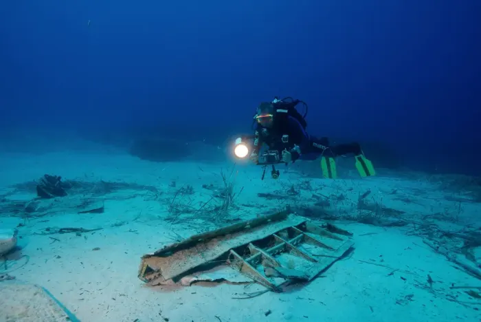 A scuba diver with a torch above wreckage on the sea floor