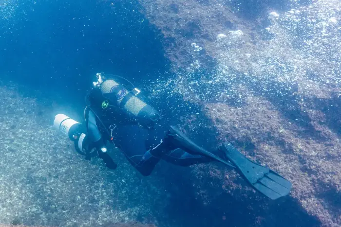 A scuba diver underwater in a wetsuit with tanks and mask