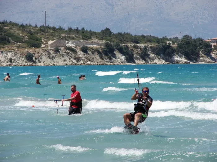 Kitesurfers riding off a windy beach, kites lined up in the sky
