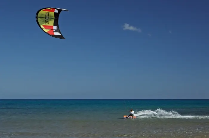 A kitesurfer riding across the water with a power kite overhead