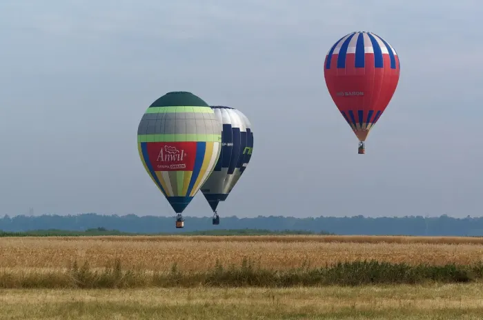 A hot air balloon inflated and rising over open countryside