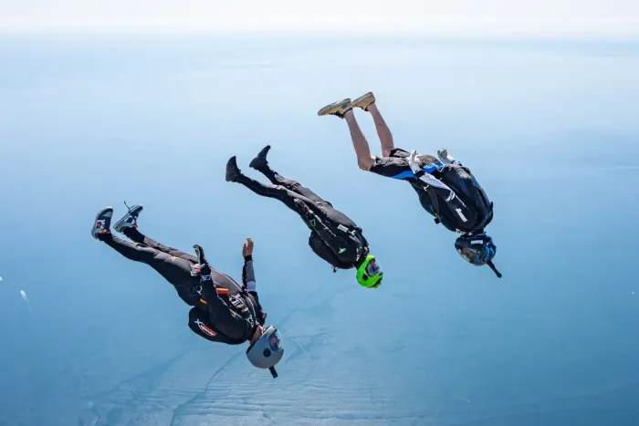 A skydiver in freefall under an open canopy above green fields