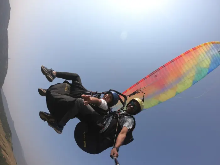 A paraglider in flight above a valley, canopy open against the sky