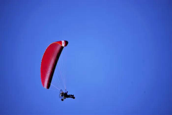 A paraglider in flight above a valley, canopy open against the sky
