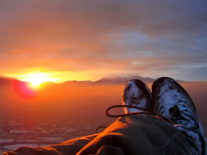 A paraglider in flight above a valley, canopy open against the sky