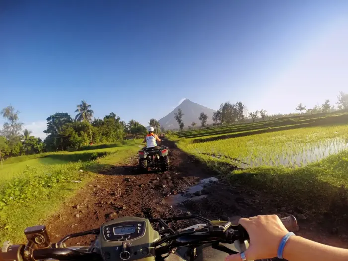 Quad bikes on a trail below a volcano, riders in helmets