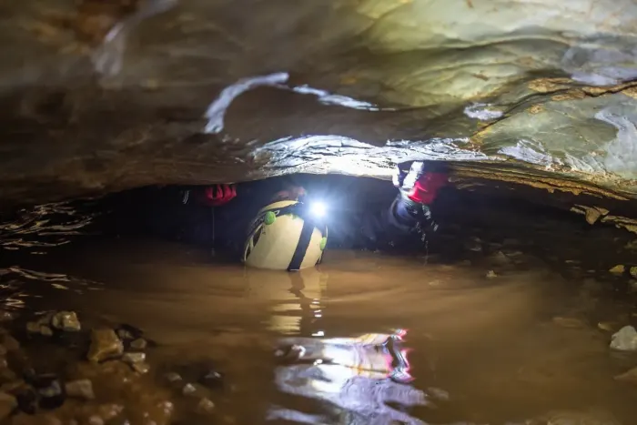 A caver with a headlamp inside a cave passage
