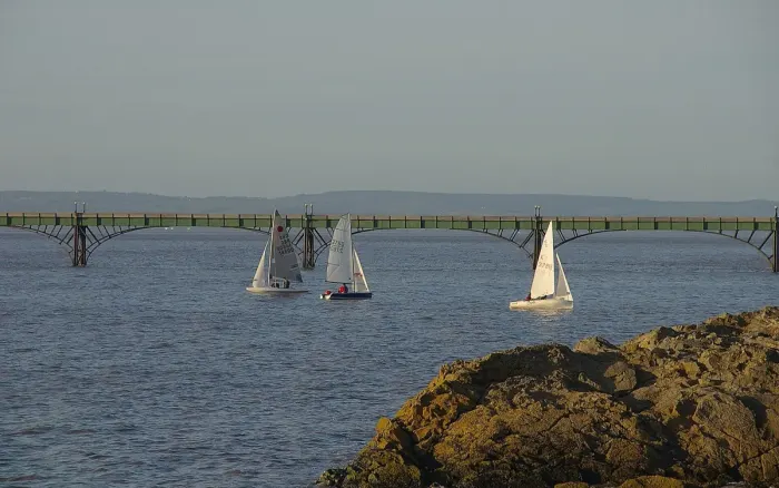 Three sailing dinghies under way near a pier