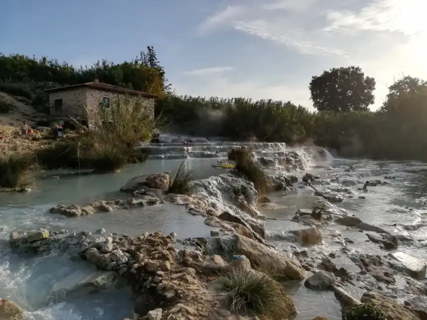 Steaming hot-spring cascades over white rock beside an old stone mill