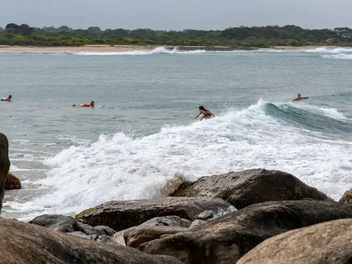 Surfers in the water beyond a rocky shore