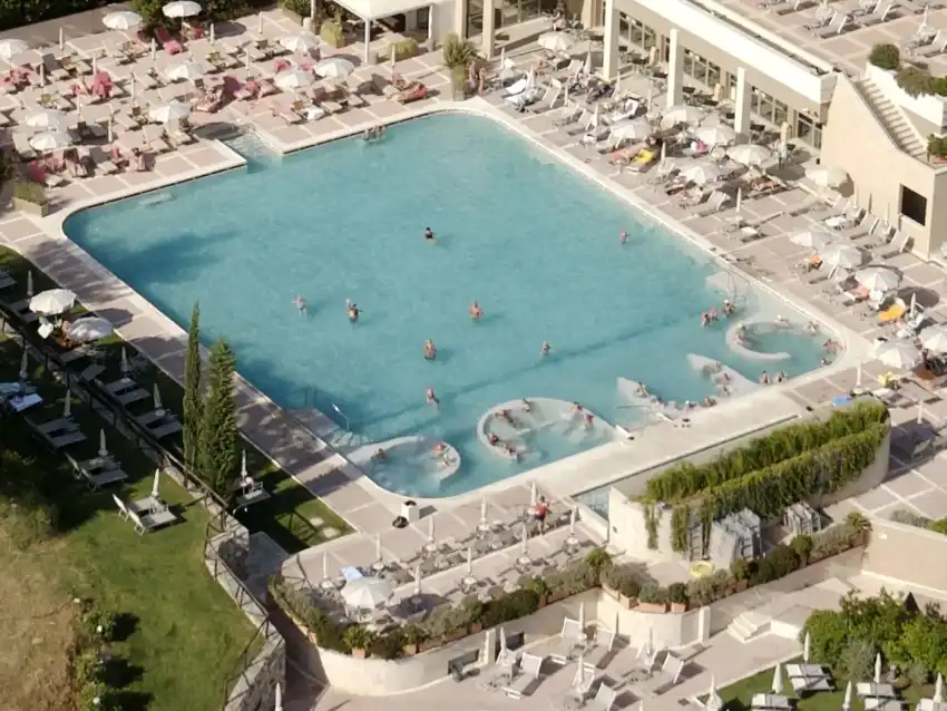 A large open-air thermal pool ringed by loungers and parasols, seen from above